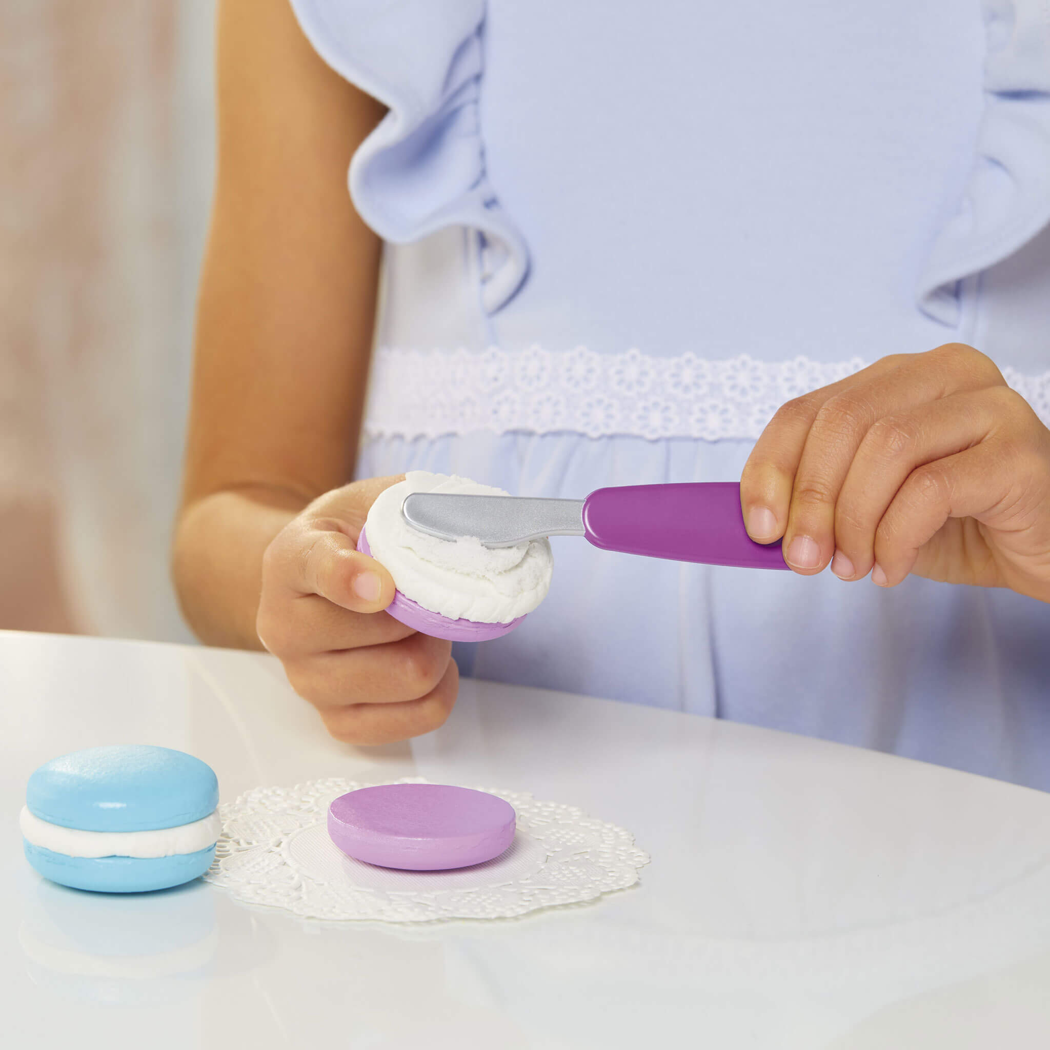 Child's hands using a purple spatula to frost toy macarons 